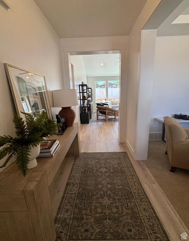 hallway with a textured ceiling and light hardwood / wood-style flooring