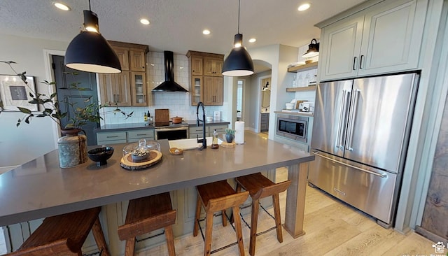 1165 N 360 E Unit 75, Salem, UT 84653 - kitchen featuring wall chimney exhaust hood, a center island with sink, light wood-type flooring, stainless steel appliances, and backsplash