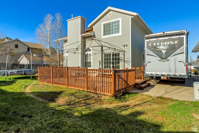 back of property featuring a trampoline, a wooden deck, a lawn, and a chimney