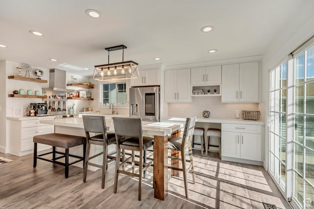 kitchen featuring stainless steel refrigerator with ice dispenser, open shelves, wall chimney exhaust hood, decorative backsplash, and recessed lighting