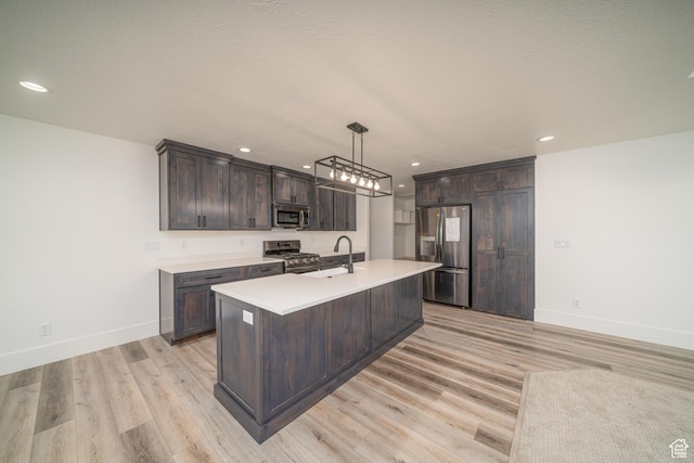 kitchen featuring dark brown cabinetry, decorative light fixtures, a center island with sink, appliances with stainless steel finishes, and light wood-type flooring