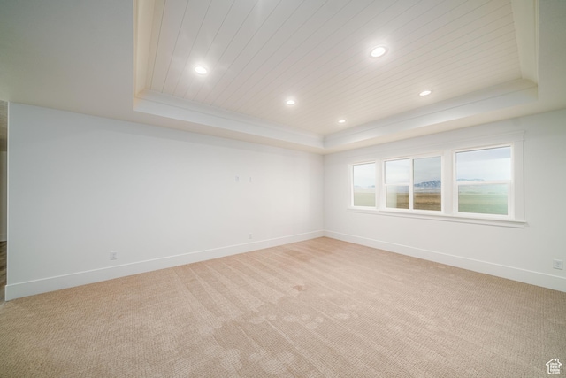 spare room with a tray ceiling, light carpet, and wood ceiling
