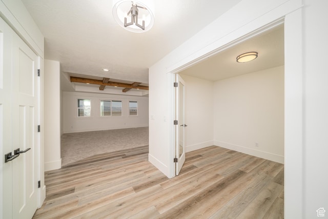 corridor with beamed ceiling, light hardwood / wood-style floors, and a chandelier