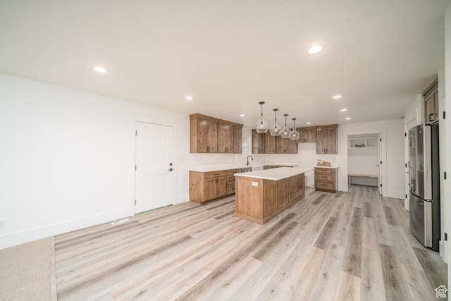 kitchen with stainless steel refrigerator, sink, decorative light fixtures, a kitchen island, and light wood-type flooring