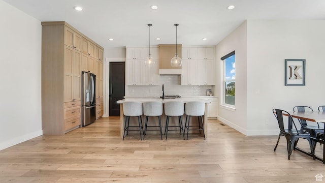 928 N Foxhunter Dr W, Farmington, UT 84025 - kitchen featuring stainless steel refrigerator with ice dispenser, a kitchen breakfast bar, light countertops, light wood finished floors, and an island with sink