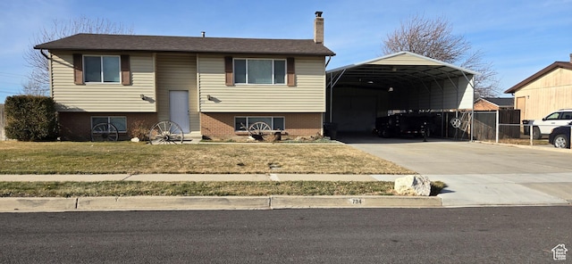 raised ranch featuring a chimney, a front lawn, driveway, a carport, and brick siding