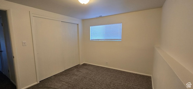 unfurnished bedroom featuring visible vents, dark carpet, and a closet