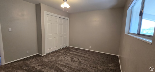 unfurnished bedroom with baseboards, a ceiling fan, dark colored carpet, and a closet