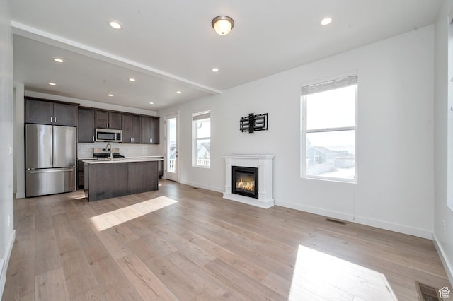 unfurnished living room featuring a glass covered fireplace, visible vents, baseboards, and a sink