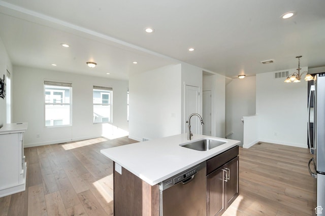 kitchen with stainless steel appliances, light countertops, a sink, light wood-style floors, and a kitchen island with sink