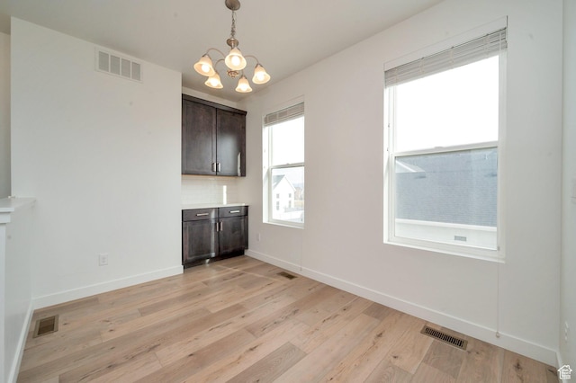 unfurnished dining area featuring a wealth of natural light, a notable chandelier, visible vents, and light wood-style flooring