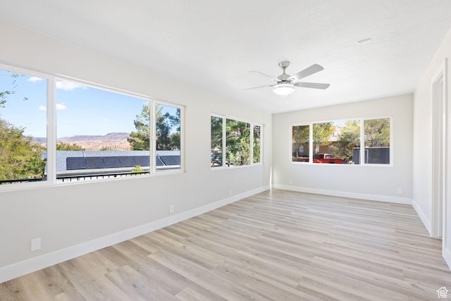 unfurnished sunroom featuring a mountain view, ceiling fan, and a healthy amount of sunlight