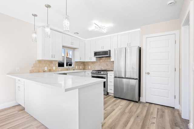 kitchen with white cabinets, kitchen peninsula, appliances with stainless steel finishes, and light hardwood / wood-style flooring