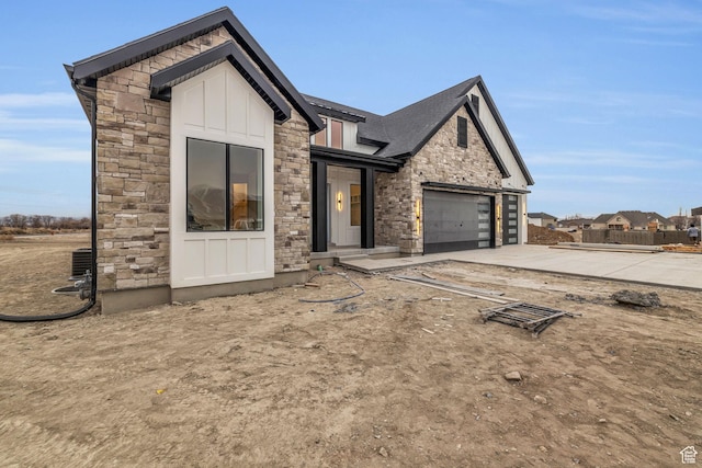 view of front of property with stone siding, driveway, board and batten siding, and cooling unit