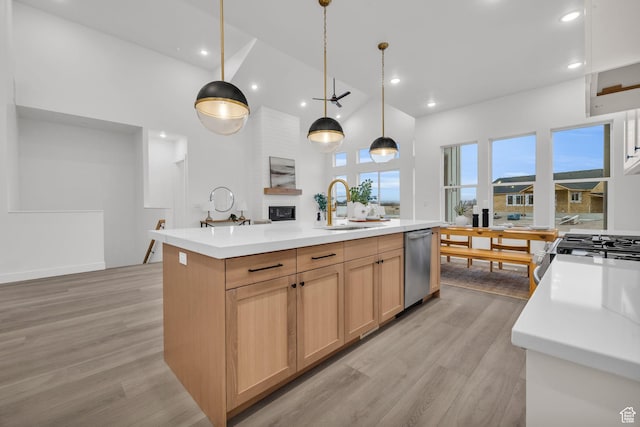 kitchen featuring a sink, appliances with stainless steel finishes, light wood-type flooring, light countertops, and a center island with sink