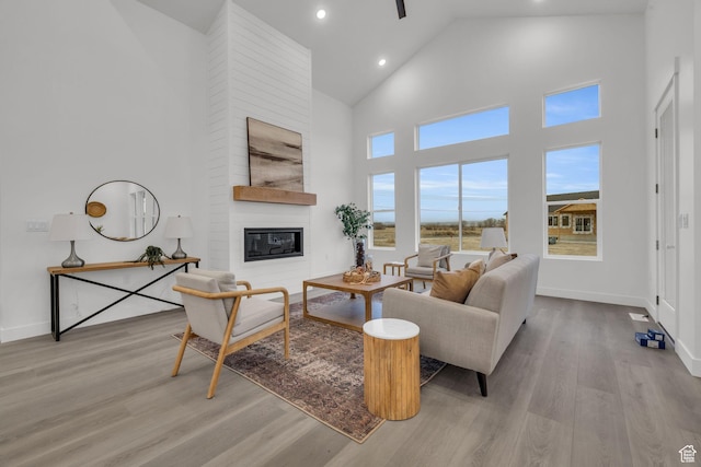 living room featuring wood finished floors, high vaulted ceiling, a fireplace, recessed lighting, and baseboards