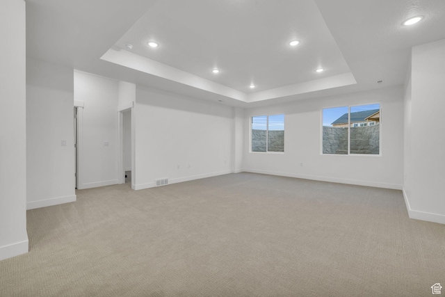 spare room with a tray ceiling, light carpet, baseboards, and recessed lighting
