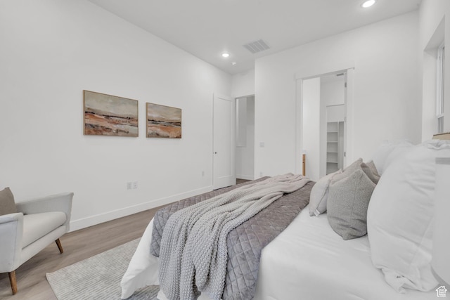 bedroom with wood finished floors, recessed lighting, baseboards, and a spacious closet