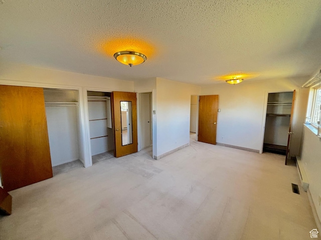 unfurnished bedroom with a textured ceiling, light carpet, two closets, and baseboards