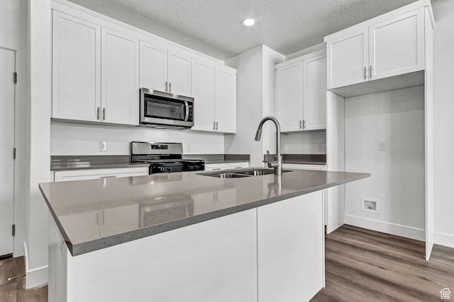 1056 E 1930 S Unit 420, Heber City, UT 84032 - kitchen featuring appliances with stainless steel finishes, a kitchen island with sink, wood finished floors, white cabinets, and a textured ceiling