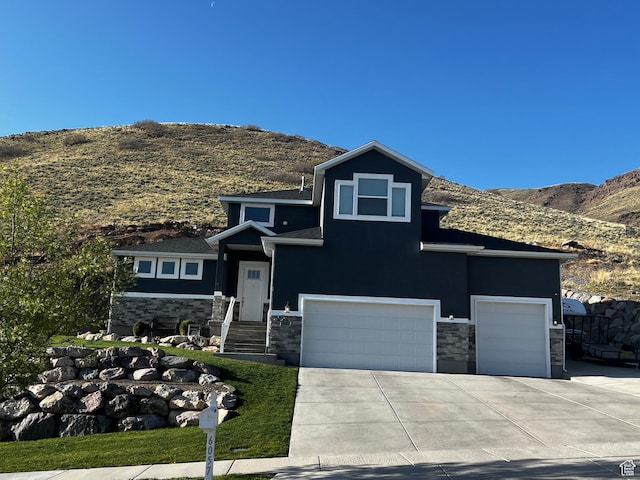 view of front of house featuring concrete driveway, stone siding, an attached garage, a mountain view, and stucco siding