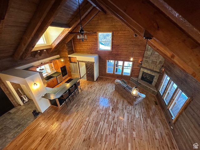 unfurnished living room with beamed ceiling, a stone fireplace, high vaulted ceiling, and light hardwood / wood-style flooring