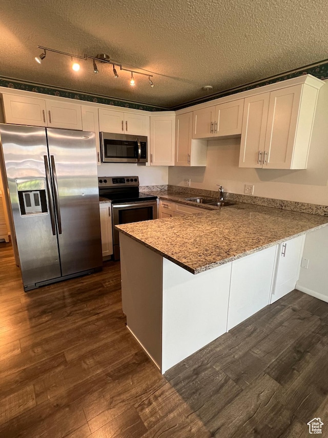 kitchen with white cabinets, dark wood finished floors, stainless steel appliances, a sink, and a peninsula