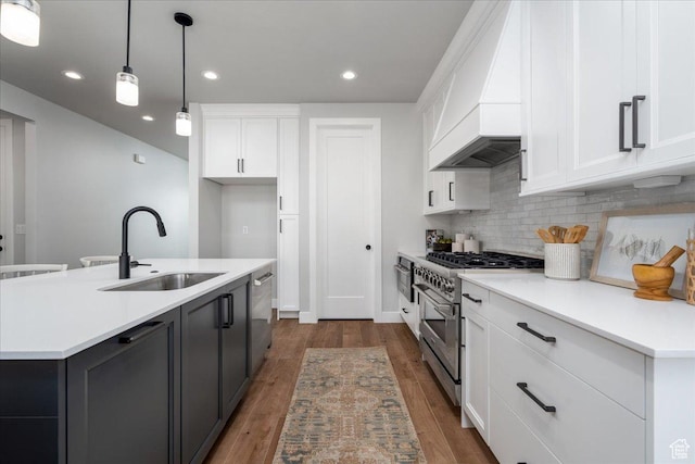 kitchen with white cabinets, wood finished floors, stainless steel appliances, a sink, and backsplash