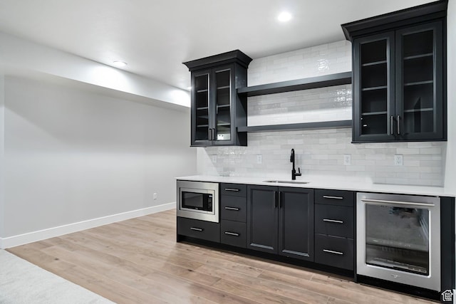 bar with tasteful backsplash, stainless steel microwave, wet bar, a sink, and beverage cooler