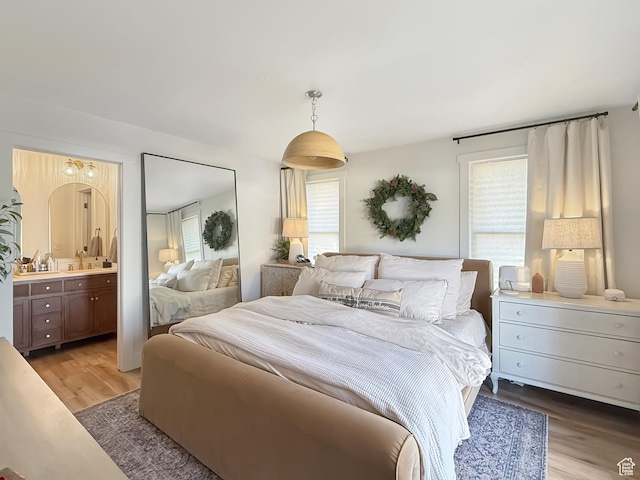 bedroom featuring light wood-style floors, ensuite bath, multiple windows, and a sink