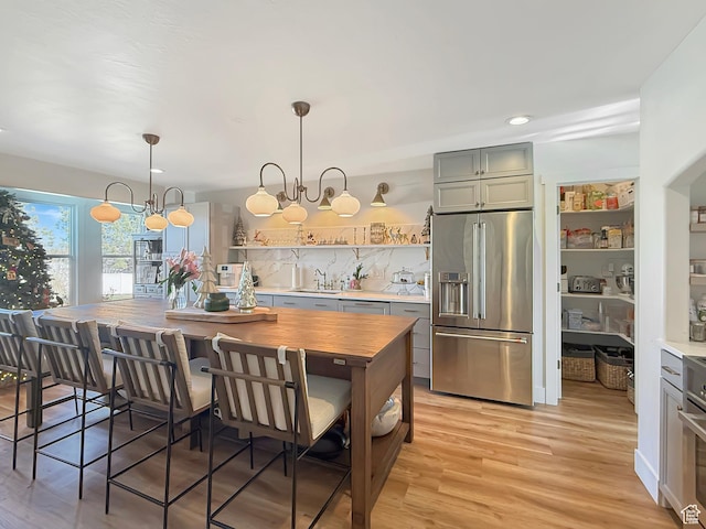kitchen with stainless steel appliances, tasteful backsplash, an inviting chandelier, light wood-style floors, and a sink