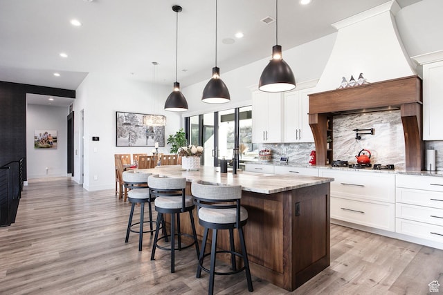 kitchen featuring decorative backsplash, light stone counters, white cabinetry, and an island with sink