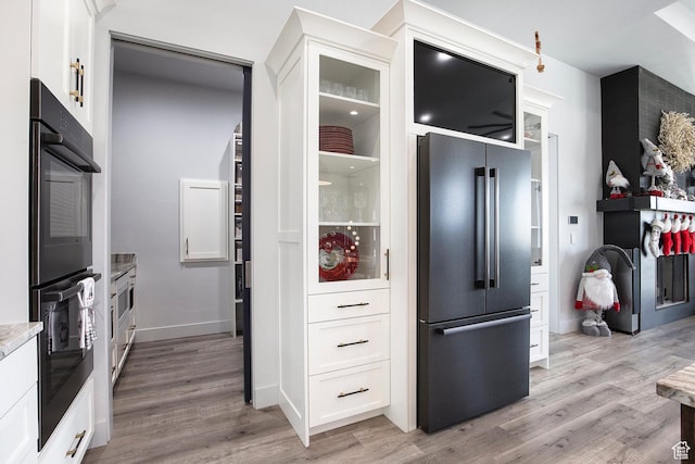 kitchen featuring high end fridge, white cabinetry, double oven, and light hardwood / wood-style flooring