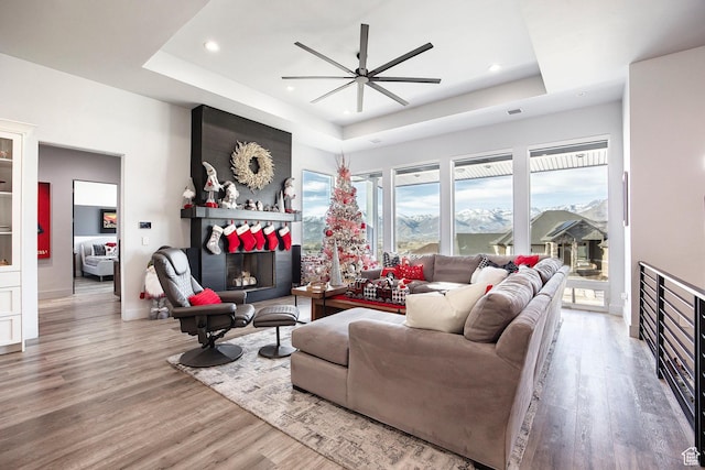 living room with a large fireplace, a tray ceiling, and hardwood / wood-style flooring