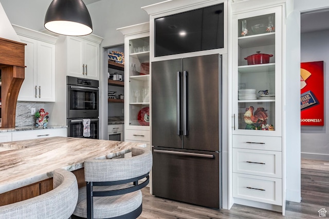 kitchen with white cabinetry, stainless steel appliances, light stone counters, decorative backsplash, and light wood-type flooring