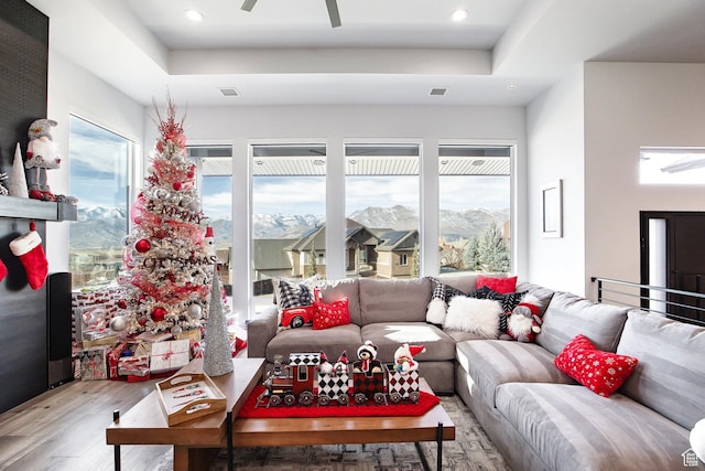 living room with a tray ceiling, a mountain view, ceiling fan, and wood-type flooring