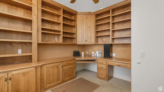 unfurnished office featuring ceiling fan, built in desk, and light carpet
