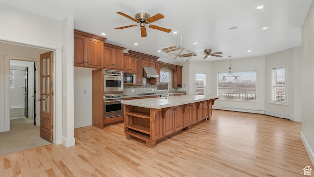 kitchen with hanging light fixtures, an island with sink, light hardwood / wood-style floors, stainless steel double oven, and black microwave