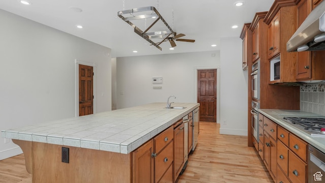 kitchen featuring exhaust hood, sink, ceiling fan, an island with sink, and tile counters