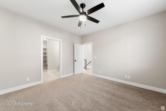 unfurnished bedroom featuring a spacious closet, a closet, ceiling fan, and light colored carpet
