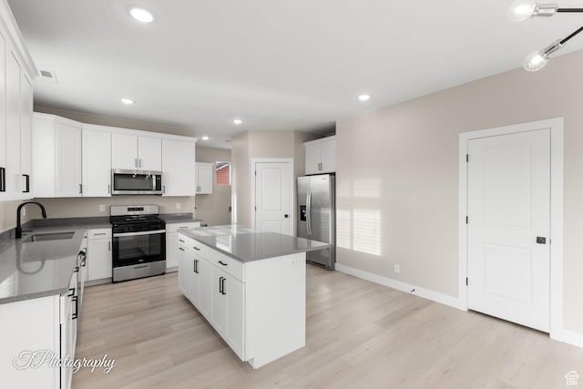 kitchen featuring sink, stainless steel appliances, a kitchen island, white cabinets, and light wood-type flooring