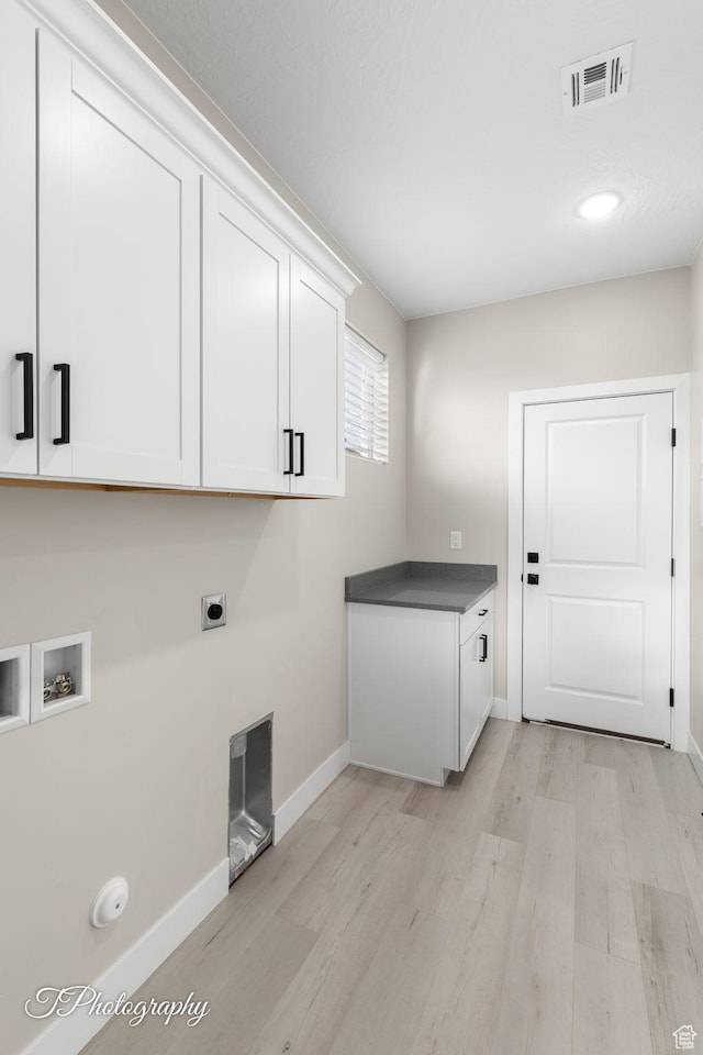 washroom with electric dryer hookup, washer hookup, cabinets, and light wood-type flooring