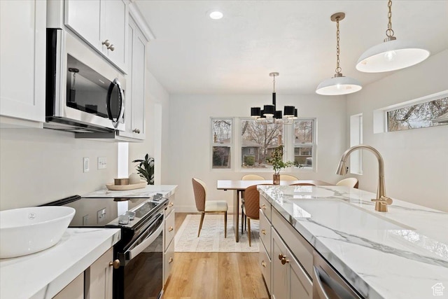 246 E 2100 S, South Salt Lake, UT 84115 - kitchen with stainless steel appliances, light wood finished floors, a chandelier, hanging light fixtures, and light stone counters