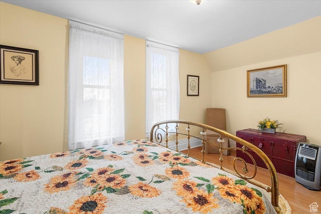bedroom with heating unit, wood-type flooring, and vaulted ceiling