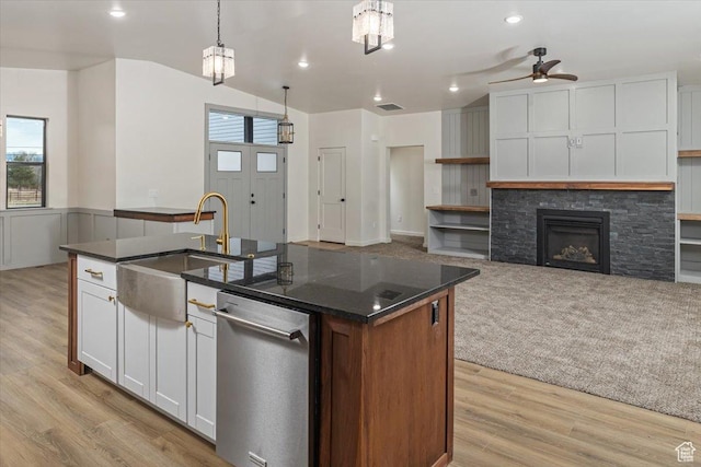 kitchen with ceiling fan, a center island with sink, white cabinets, a stone fireplace, and hanging light fixtures