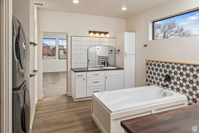 bathroom featuring hardwood / wood-style floors, vanity, stacked washer / dryer, and a wealth of natural light