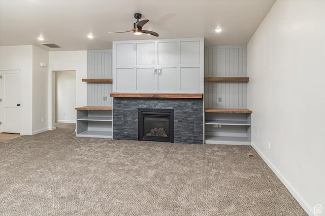 unfurnished living room with light colored carpet, a stone fireplace, and ceiling fan