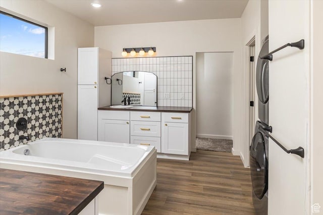 bathroom featuring vanity, stacked washing maching and dryer, hardwood / wood-style flooring, and a bathing tub