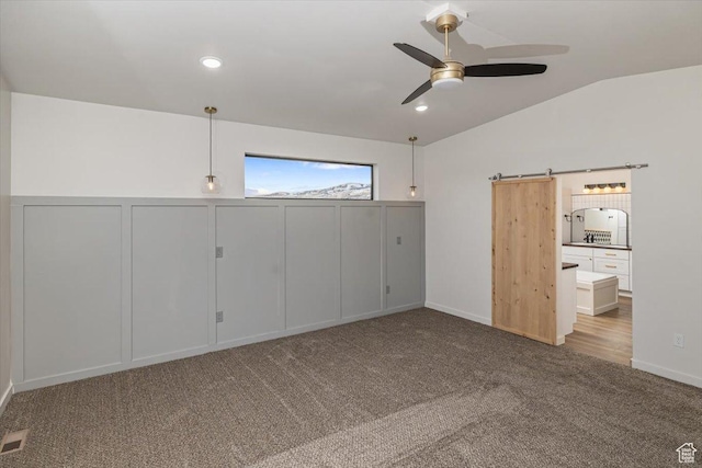 unfurnished bedroom with light carpet, a barn door, ceiling fan, and lofted ceiling