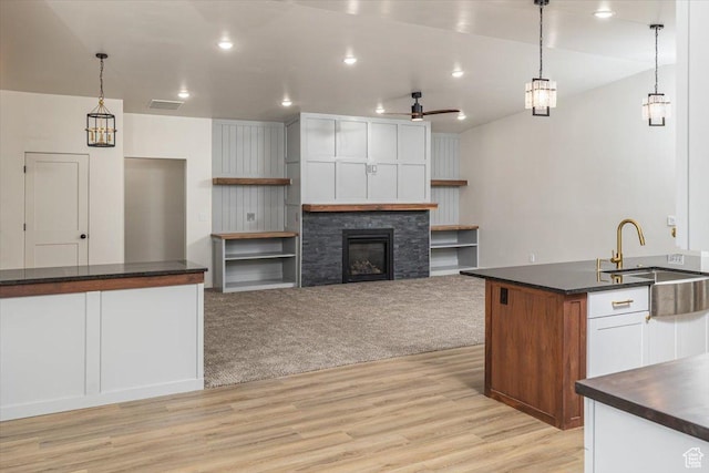 kitchen with ceiling fan, sink, white cabinetry, hanging light fixtures, and a stone fireplace